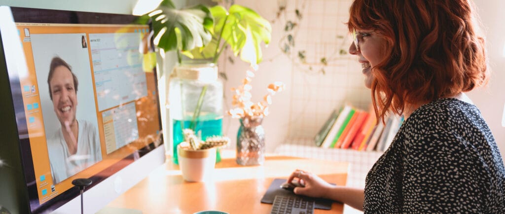 Young woman sitting in front of a computer screen, engaging with an attendee during a virtual conference.